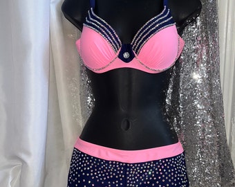 May include: A pink and navy blue two-piece swimsuit with rhinestones. The top is a push-up bra style with a navy blue trim and rhinestones. The bottom is a high-waisted short with a pink waistband and rhinestones.