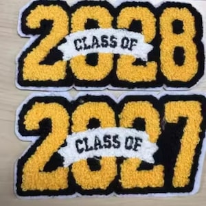 May include: Two chenille patches featuring the numbers 2028 and 2027 in yellow with black outlines. Each patch includes a white banner across the center with the black text "CLASS OF" embroidered on it, finished with a white border edge.