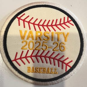 May include: Circular baseball patch with a cream-colored background, red stitching, and black and white border. The patch features the words "VARSITY 2025-26 BASEBALL" in gold lettering, and red stitching that mimics a baseball.