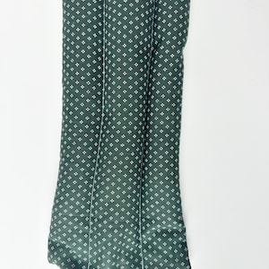 May include: A rectangular, dark green fabric cushion featuring a repeating pattern of small, white four-dot clusters. The cushion is divided into three vertical, padded sections by two parallel stitched lines running the length of the item.