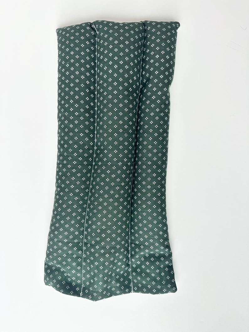May include: A rectangular, dark green fabric cushion featuring a repeating pattern of small, white four-dot clusters. The cushion is divided into three vertical, padded sections by two parallel stitched lines running the length of the item.