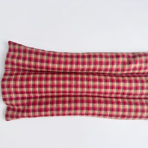 May include: A rectangular fabric heating pad featuring a red and tan plaid pattern. The item is constructed with three horizontal, stitched channels that create a segmented, elongated shape, providing a consistent texture across the surface.