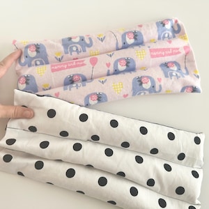 May include: Two rectangular fabric items. One is pink with a pattern of blue elephants, flowers, and the text "mummy and me". The other is white with large black polka dots. The items appear to be filled.