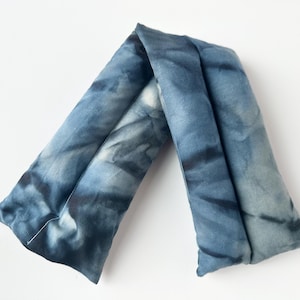 May include: A blue tie-dye neck wrap, designed to provide comfort. The wrap is made of soft fabric and features a unique pattern of dark and light blue hues. The wrap is folded in a V-shape.