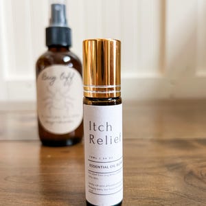 May include: Two amber glass bottles with white labels. The front bottle is a roll-on labeled "Itch Relief" with a gold cap. The back bottle is a spray bottle labeled "Bug Off". Both bottles contain essential oil blends.