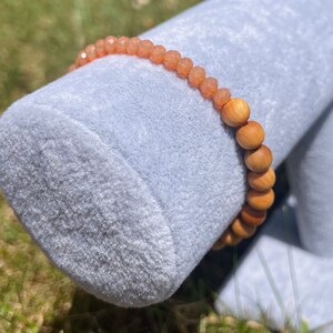 May include: A bracelet made of light orange gemstone beads and brown wooden beads. The bracelet is displayed on a light blue velvet surface.