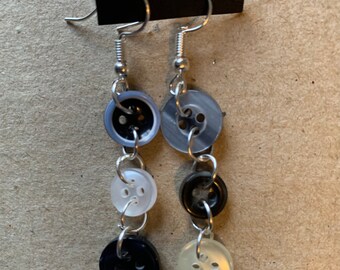 May include: A pair of dangle earrings with a silver chain and four buttons. The buttons are black, white, and gray.