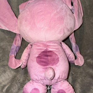 Puede incluir: Un peluche rosa con orejas grandes y un dise&ntilde;o en forma de coraz&oacute;n en la espalda. El juguete tiene un cuerpo redondeado, pies grandes y una peque&ntilde;a cola. Las orejas tienen detalles morados.