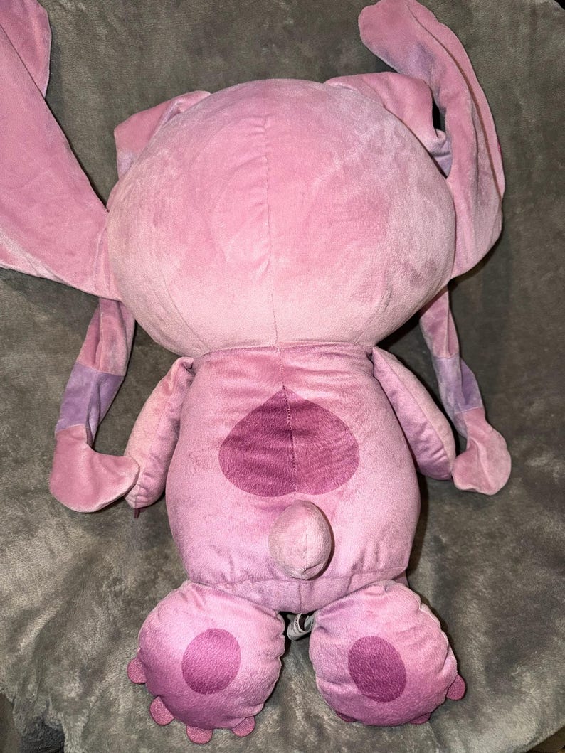 Puede incluir: Un peluche rosa con orejas grandes y un dise&ntilde;o en forma de coraz&oacute;n en la espalda. El juguete tiene un cuerpo redondeado, pies grandes y una peque&ntilde;a cola. Las orejas tienen detalles morados.