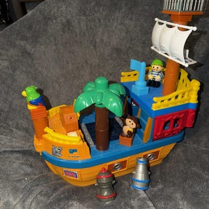 May include: A colorful Mega Bloks pirate ship playset featuring a yellow hull, blue deck, and a brown mast with a white sail. The set includes a green palm tree, a parrot, a monkey, and two small figures, along with two separate gray accessories.
