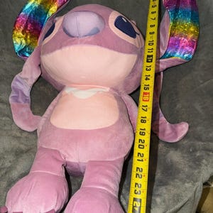 Puede incluir: Un mu&ntilde;eco de peluche de color lavanda de Angel con grandes orejas con tela iridiscente de arco&iacute;ris. El mu&ntilde;eco mide aproximadamente 66 cm de alto. Tiene ojos azules grandes y un pecho rosa claro.