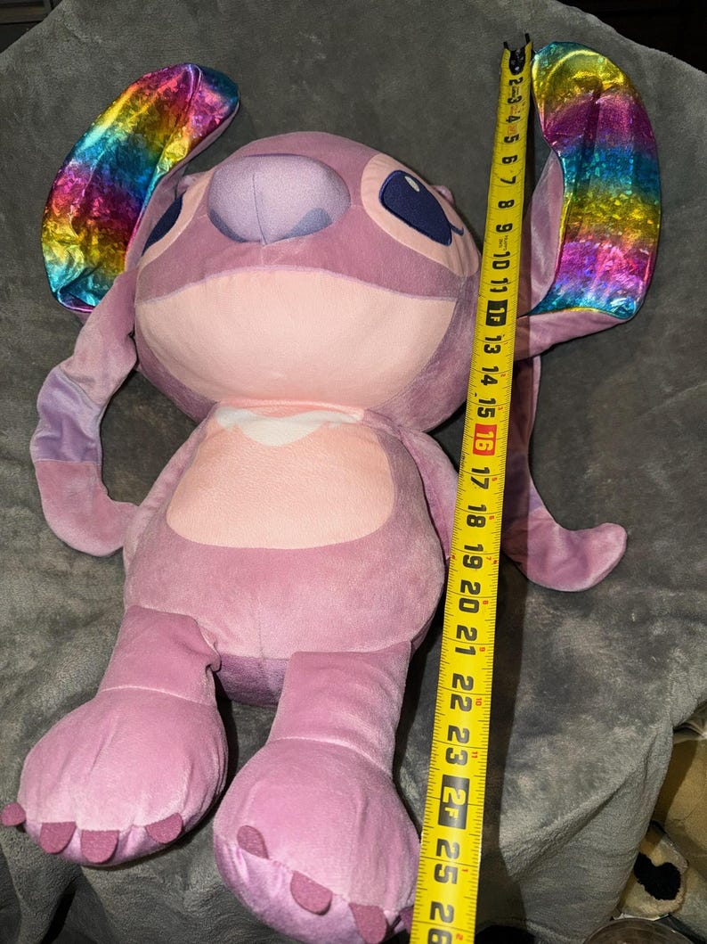 Puede incluir: Un mu&ntilde;eco de peluche de color lavanda de Angel con grandes orejas con tela iridiscente de arco&iacute;ris. El mu&ntilde;eco mide aproximadamente 66 cm de alto. Tiene ojos azules grandes y un pecho rosa claro.