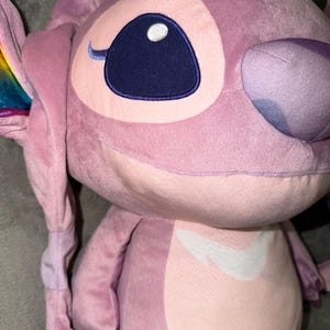 Puede incluir: Un peluche rosa del personaje Angel de Lilo & Stitch. El juguete presenta grandes ojos azules, una marca blanca en el pecho y acentos de arco&iacute;ris en las orejas. Un juguete suave y tierno.