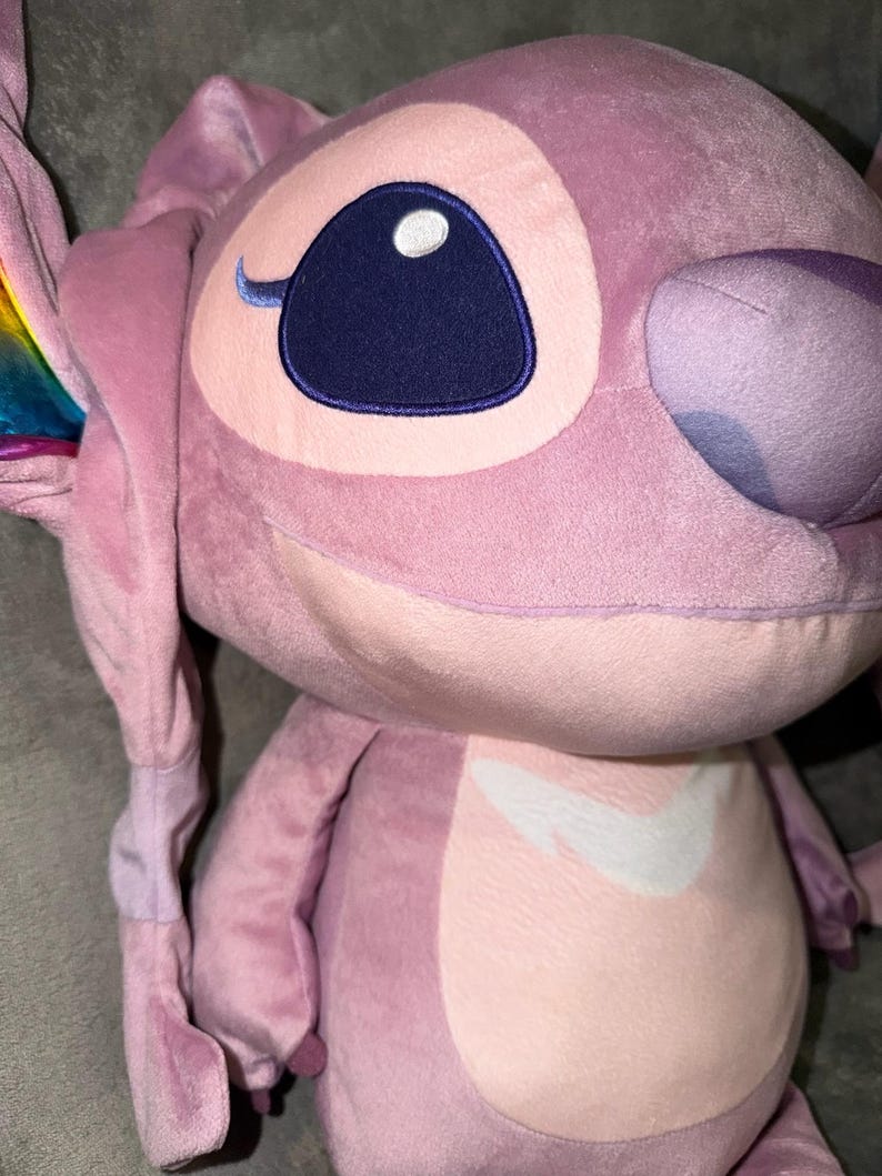 Puede incluir: Un peluche rosa del personaje Angel de Lilo & Stitch. El juguete presenta grandes ojos azules, una marca blanca en el pecho y acentos de arco&iacute;ris en las orejas. Un juguete suave y tierno.