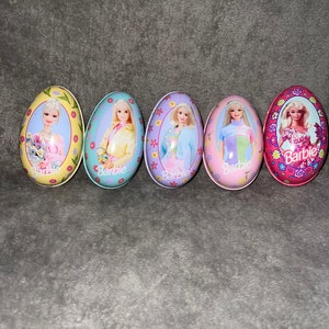 May include: Five colorful plastic Easter eggs with a Barbie doll image on each. The eggs are decorated with flowers and the word "Barbie" is printed on each egg.