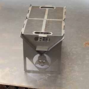 May include: A silver folding grill with a Darth Vader design. The grill has a rectangular cooking surface with a grid pattern.