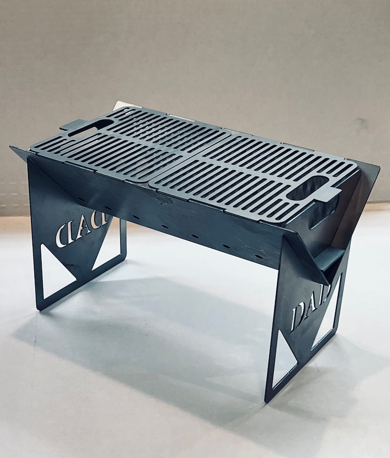 May include: A portable, stainless steel grill with a folding design. The grill has a rectangular cooking surface with a grid pattern and two handles. The grill is supported by two triangular legs with the words "CIAC" and "DAD" cut out.