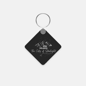May include: Black square keychain with a white mountain range design and the text "Velaris The City of Starlight".