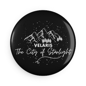 May include: Black and white button with a mountain range and trees, with the text "VELARIS The City of Starlight" in a white cursive font.
