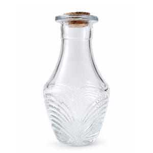 May include: A clear glass bottle with a wide, rounded base that tapers toward a narrow neck and a flared rim. The lower portion of the bottle features a textured, fan-like embossed pattern. A cylindrical brown cork stopper sits in the opening.