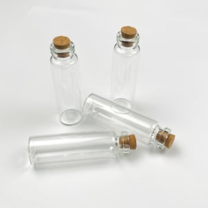 May include: Three clear glass bottles with cork stoppers. The bottles are lying on a white surface.