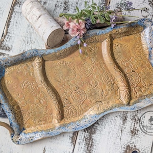 May include: A rectangular ceramic serving tray with a gold-colored interior and a blue rim. The tray features a floral and honeycomb pattern. It has two gold handles and is approximately 16 inches long.