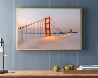 May include: A framed photograph of the Golden Gate Bridge in San Francisco, California. The bridge is lit up at night and is covered in fog. The photo is taken from a low angle, giving the viewer a sense of scale.