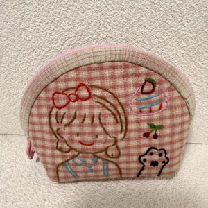 May include: A pink and white gingham patterned coin purse with a zipper closure. The purse features an embroidered illustration of a girl with a bow, a cupcake, cherries, and a paw print.