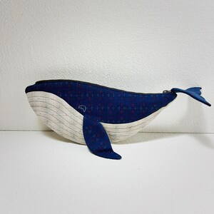 K&ouml;nnte beinhalten: Eine blaue und wei&szlig;e, walf&ouml;rmige Rei&szlig;verschlusstasche mit einem roten und blauen gemusterten Stoff. Die Tasche ist aus Stoff und hat einen Rei&szlig;verschluss.