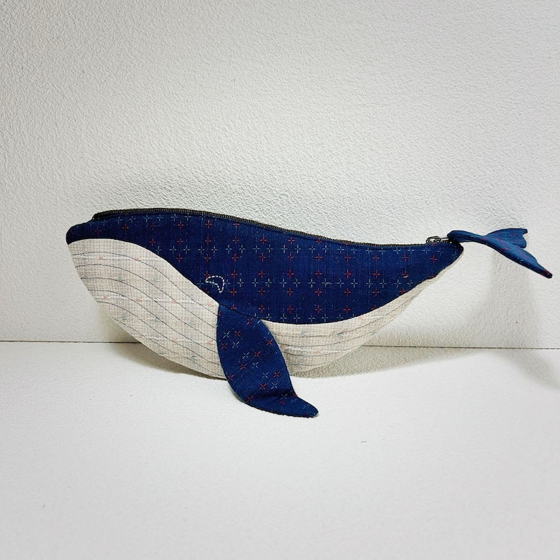 K&ouml;nnte beinhalten: Eine blaue und wei&szlig;e, walf&ouml;rmige Rei&szlig;verschlusstasche mit einem roten und blauen gemusterten Stoff. Die Tasche ist aus Stoff und hat einen Rei&szlig;verschluss.