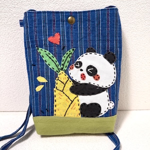 May include: Blue fabric crossbody bag with a panda bear applique hugging a bamboo stalk. The bag features a red heart, green leaves, and yellow bamboo. The bag has a green base and a button closure.