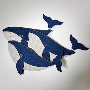 Puede incluir: Tres estuches con cremallera en forma de ballena azul y blanca con un tejido estampado azul y blanco. Los estuches están apilados uno encima del otro.