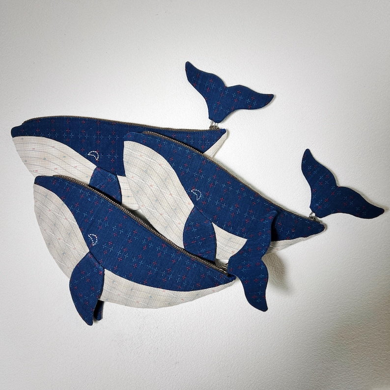 K&ouml;nnte beinhalten: Drei blaue und wei&szlig;e, rei&szlig;verschlussversehene Beutel in Walform mit einem blauen und wei&szlig;en gemusterten Stoff. Die Beutel sind &uuml;bereinander gestapelt.