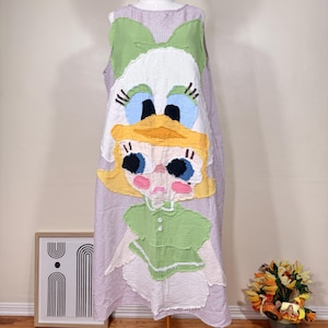 May include: A sleeveless, lilac and white checkered dress featuring a large, whimsical Daisy Duck applique. The applique includes a green bow, white head, blue eyes, yellow beak, and a green top. The dress is displayed on a mannequin.