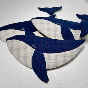 K&ouml;nnte beinhalten: Drei blaue, walf&ouml;rmige Rei&szlig;verschlusstaschen mit wei&szlig;em und blauem Muster. Die Taschen sind aus einem weichen, strukturierten Stoff gefertigt und haben einen Rei&szlig;verschluss.