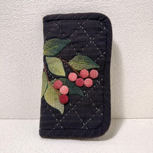 Puede incluir: Estuche rectangular acolchado en azul marino oscuro, con un patrón de diamantes cosidos. El estuche está adornado con una aplicación de hojas verdes y bayas rosas y rojas. Los bordes están cuidadosamente acabados.