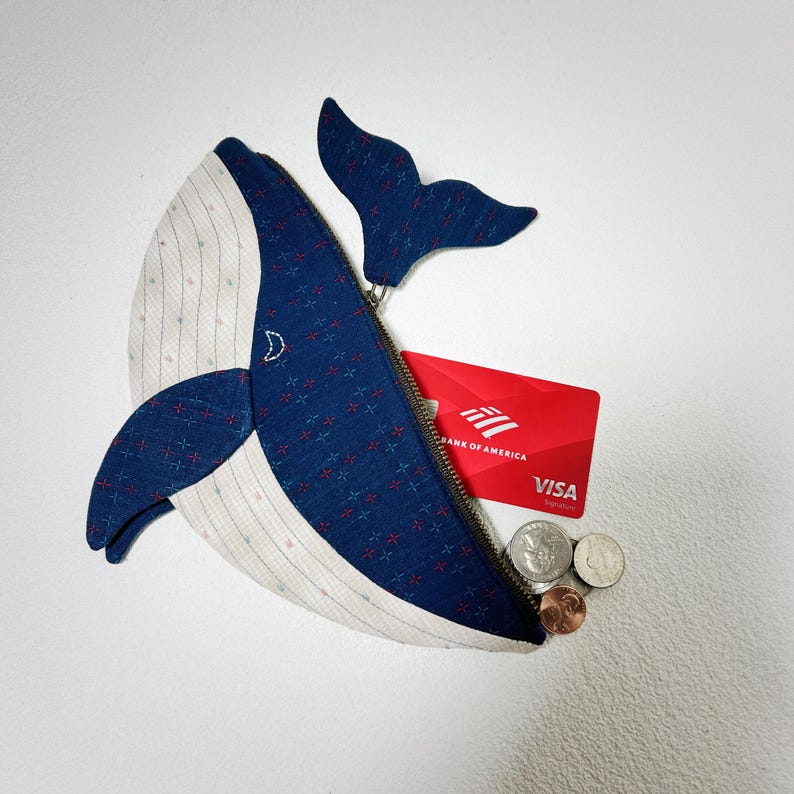 K&ouml;nnte beinhalten: Eine blaue und wei&szlig;e, walf&ouml;rmige Rei&szlig;verschlusstasche mit einer roten Kreditkarte darin, auf der "Bank of America VISA" steht.