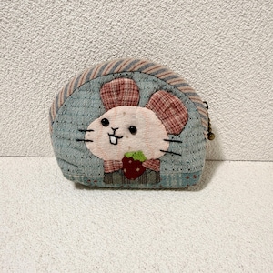 May include: A small, round coin purse made of light blue quilted fabric. It features an appliqued design of a smiling mouse with plaid ears and a strawberry. The top edge has a striped pattern.