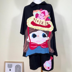 Könnte beinhalten: Schwarzes, übergroßes T-Shirt mit einem skurrilen Applikationsdesign. Das Design zeigt ein Cartoon-Mädchen, das einen Hut mit bunten Eiscremes und einer roten Schleife trägt. Das Shirt hat einen Kragen und kurze Ärmel.