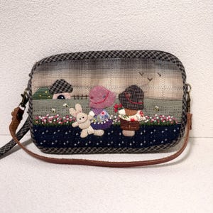 Può includere: Borsa a tracolla fatta a mano con una scena stravagante. La borsa presenta un design patchwork con un paesaggio di una casa, fiori e figure. Un cinturino marrone e un motivo a scacchi sulla parte superiore completano il design.
