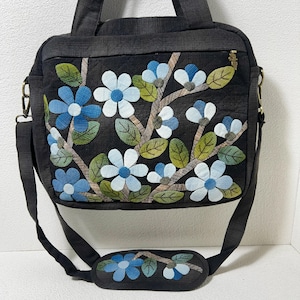 Peut inclure: Sac à bandoulière matelassé noir avec un motif floral. Le sac présente un motif de fleurs bleues et blanches avec des feuilles vertes et des branches marron. Il possède une poignée supérieure, une bandoulière amovible et un repose-épaule rembourré avec broderie florale assortie.