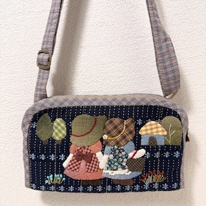 Puede incluir: Bolso de hombro a cuadros azul y rosa con un diseño caprichoso. El bolso presenta una escena bordada con dos figuras tomadas de la mano, árboles y una pequeña casa. La correa es ajustable y el bolso tiene cierre de cremallera.