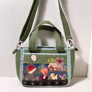 Op de afbeelding: Een gewatteerde tas met groen-wit vichy-ruitpatroon en een afneembare schouderriem. De voorzijde toont een stoffen applicatie van twee figuren met hoeden, een klein huisje, een hond en een ballon op een donker paneel van stof.