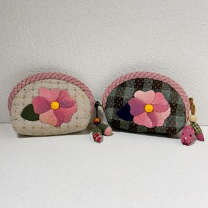 Puede incluir: Dos monederos de tela rosa y marrón con diseños de flores. Los monederos están hechos de tela de patchwork y tienen un patrón de cuadros rosa y blanco.