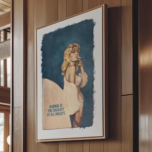 May include: A framed vintage-style print featuring a blonde woman in a white robe against a blue backdrop. The print, in a gold frame, is mounted on a wood-panelled wall. The text on the print reads "NORMAL IS THE CRUELEST OF ALL INSULTS."