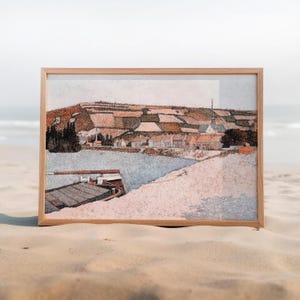 May include: A framed print of a coastal village scene. The artwork shows a village beside water, with a boat in the foreground. The colour palette includes shades of brown, beige, and blue, creating a serene and rustic aesthetic.