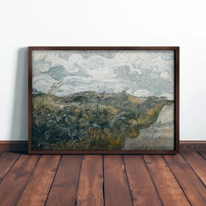 May include: A framed landscape painting with a dark brown wooden frame. The artwork depicts a field with tall grass and a cloudy sky. The color palette includes shades of green, yellow, and gray.