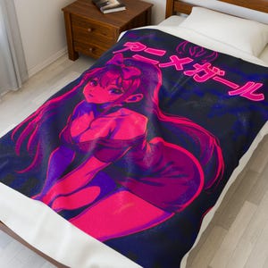 Könnte beinhalten: Eine Decke mit einer Anime-Illustration in Pink- und Lilatönen auf einem dunkelblauen Hintergrund. Japanischer Text ist oben zu sehen. Die Decke liegt auf einem Bett mit einem weißen Laken. Das Design ist auffällig.