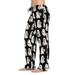 May include: Black pajama pants with a repeating pattern of white cartoon ghosts reading books. The ghosts have a simple design with a white body, black eyes, and are holding books of various colors. The pants have a drawstring waist.
