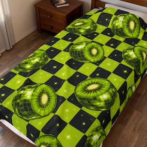 Könnte beinhalten: Eine grün-schwarz karierte Decke mit einem sich wiederholenden Muster aus Discokugel-Kiwis. Die Kiwis sind halbiert und zeigen das Innere der Frucht. Die Decke liegt auf einem Bett.